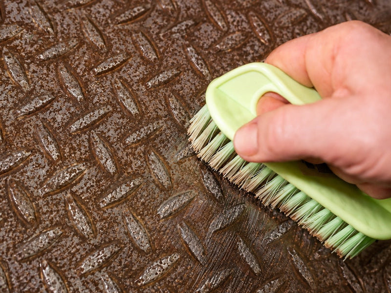 Scrubbing loose rust off a steel plate with a stiff brush